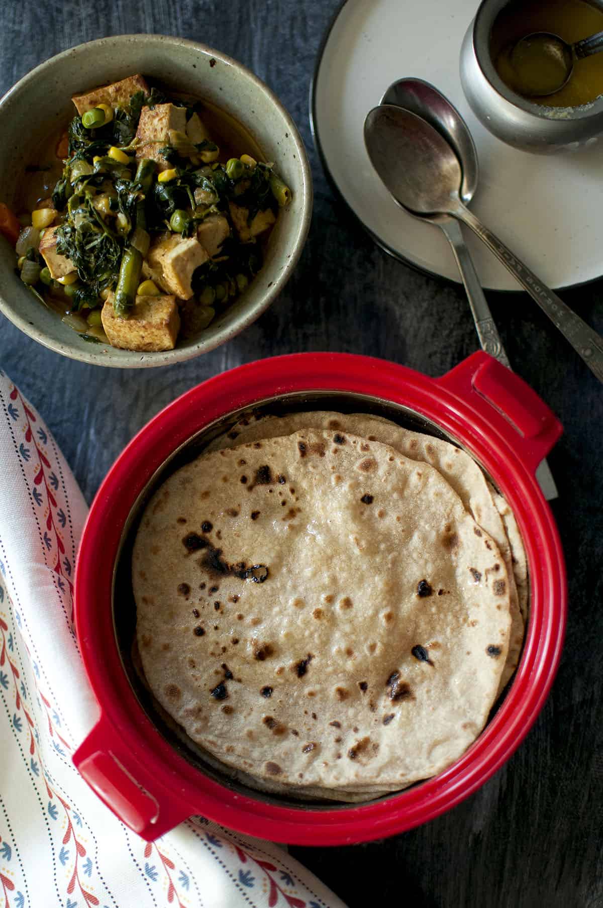 Red Casserole dish with freshly made chapatti and a vegetable curry on the side