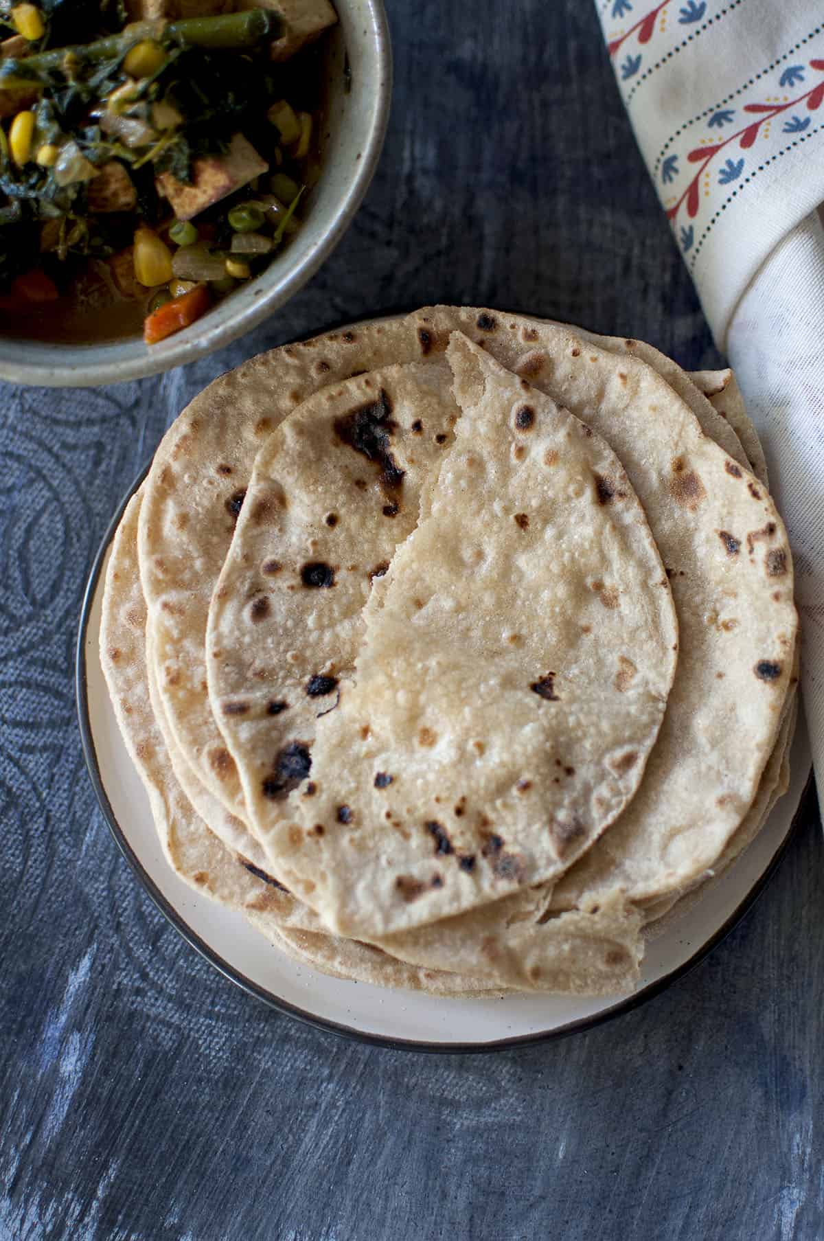 White plate with a stack of Indian flatbread and a half on top