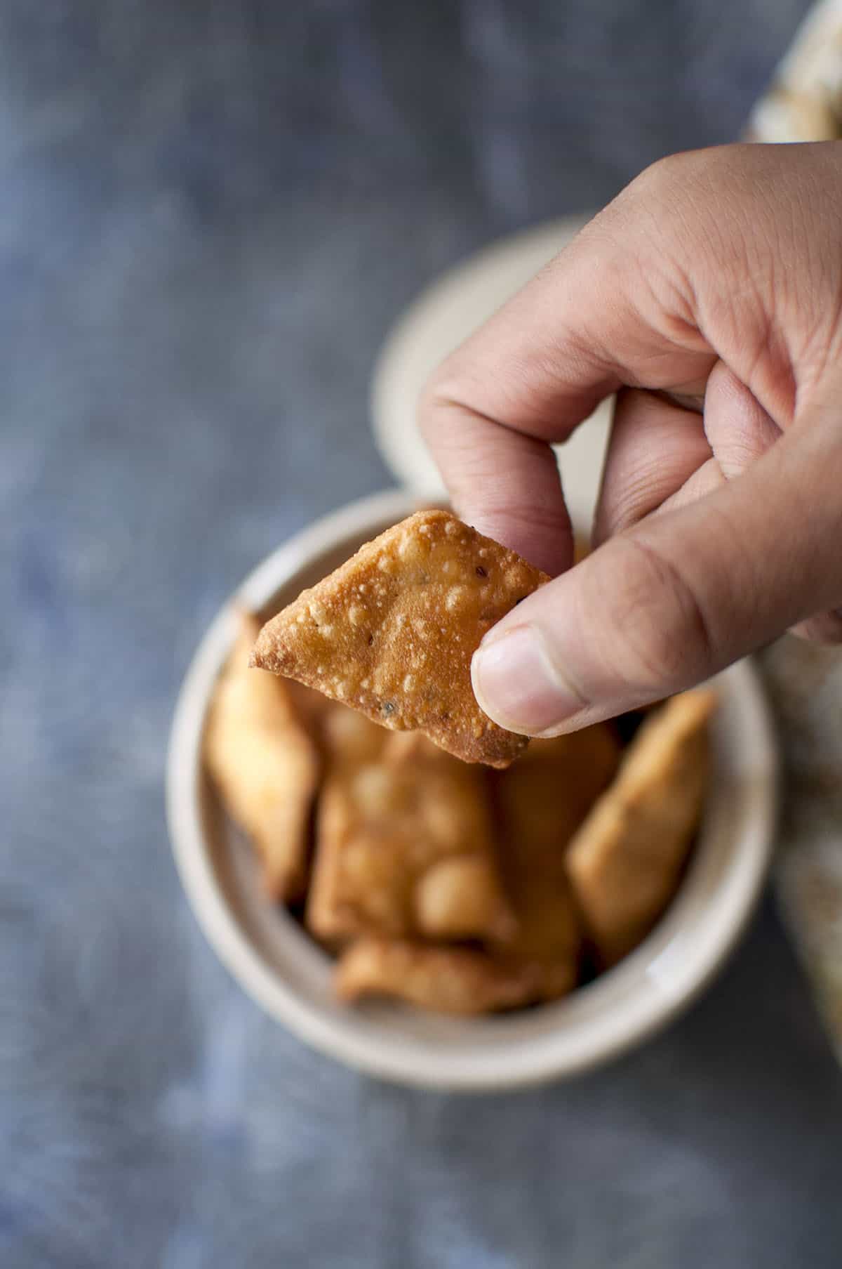 Hand holding a crispy namkeen with a bowl of them in the background