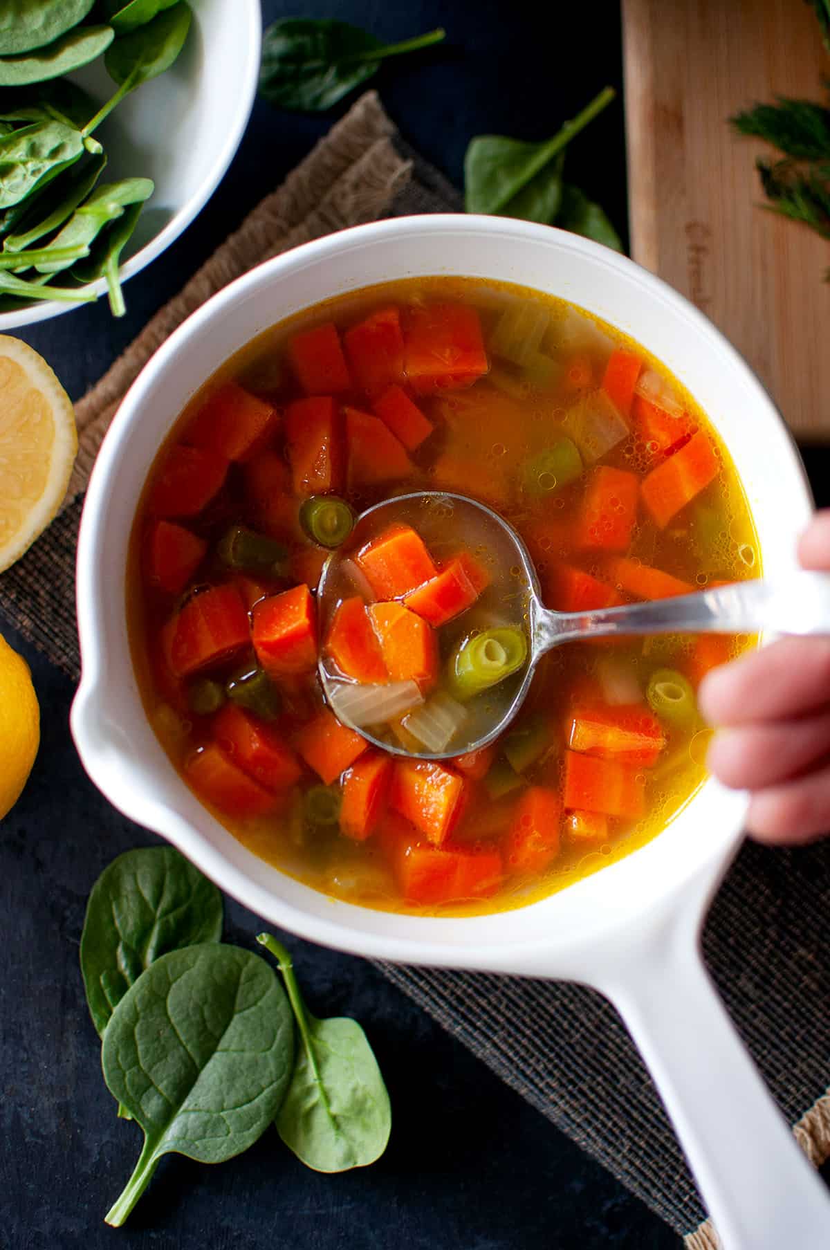 Hand holding a ladle in a bowl with carrot green bean soup.