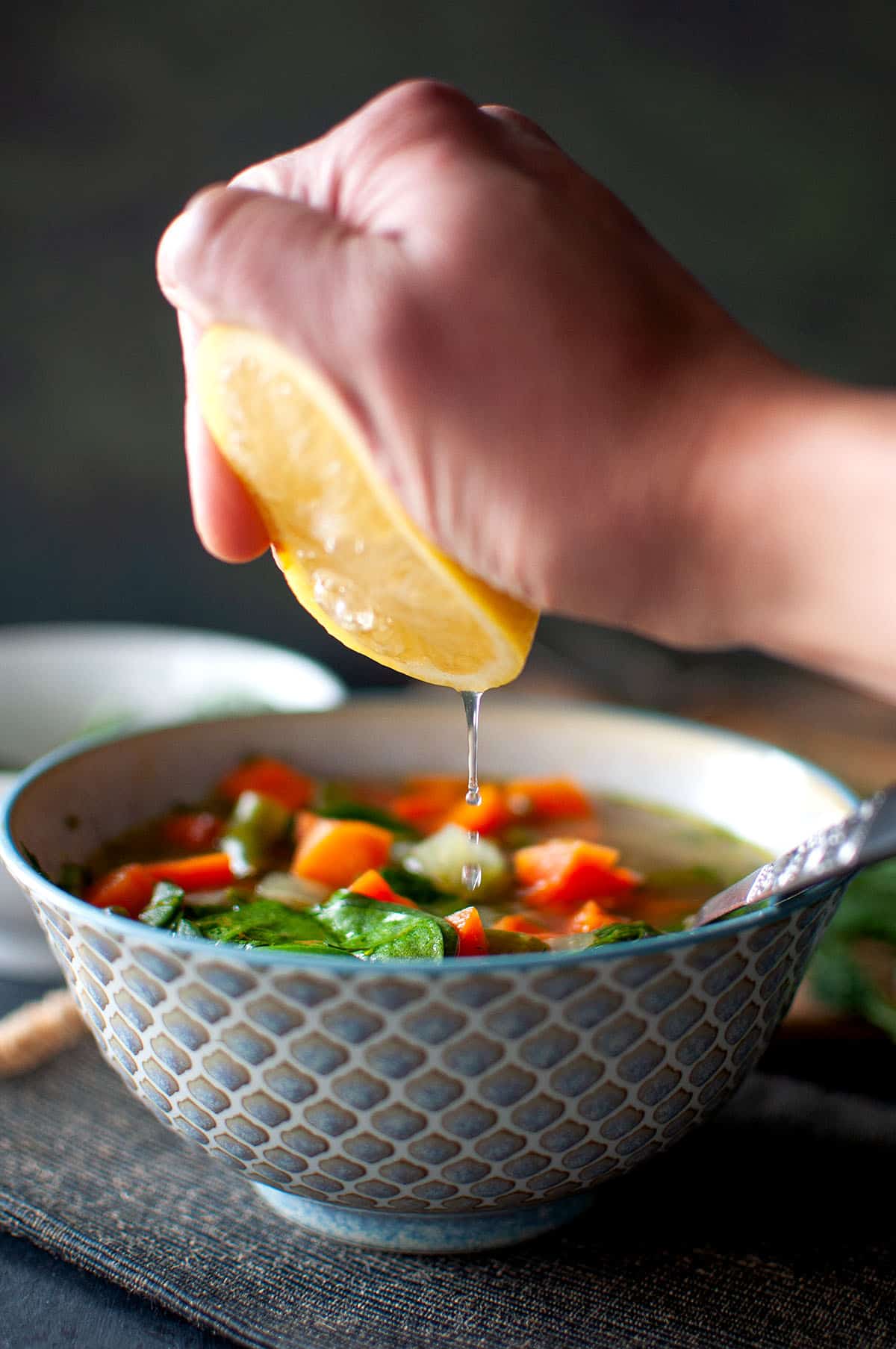 Hand squeezing lemon juice into a bowl of soup.