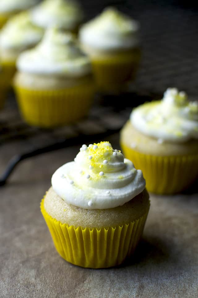 Vegan lemon cupcake in a yellow cupcake liner topped with frosting and sprinkles