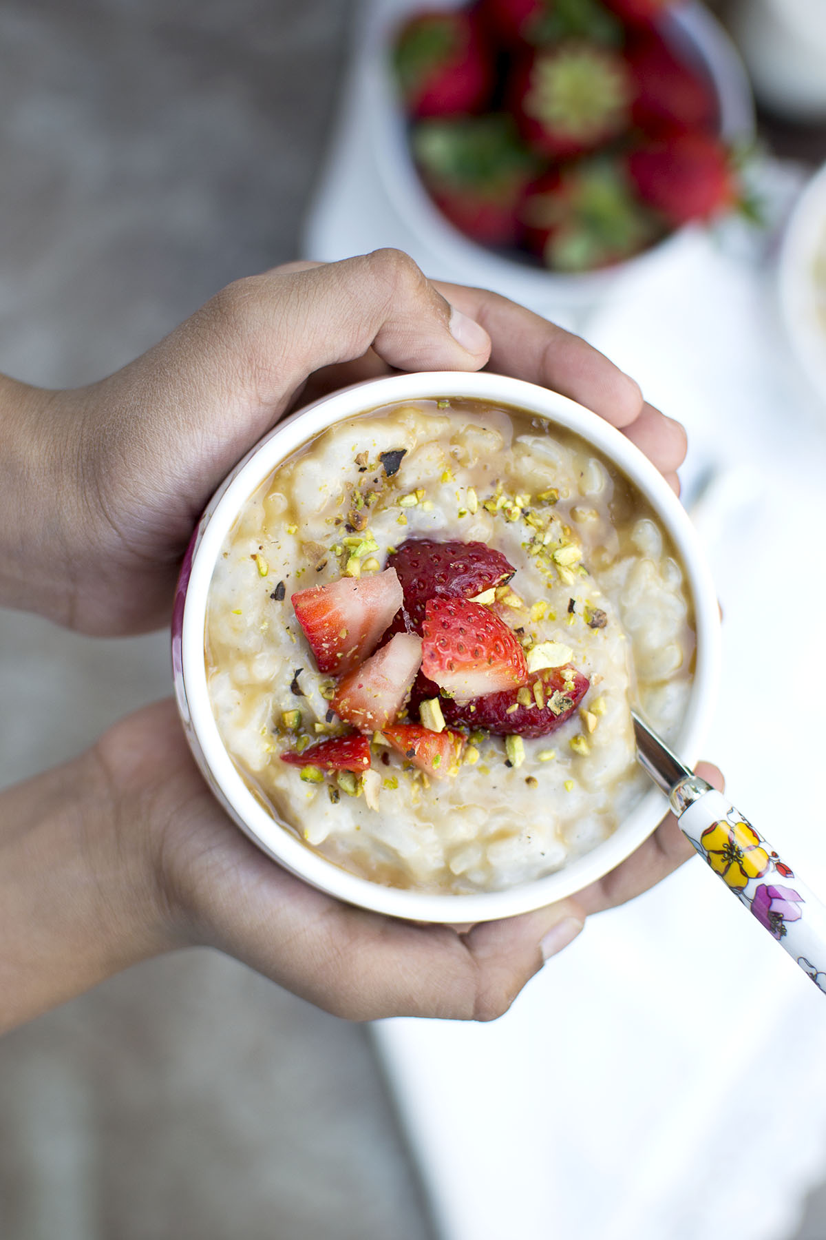 Hands holding a bowl with Almond rice pudding topped with strawberries and chopped nuts