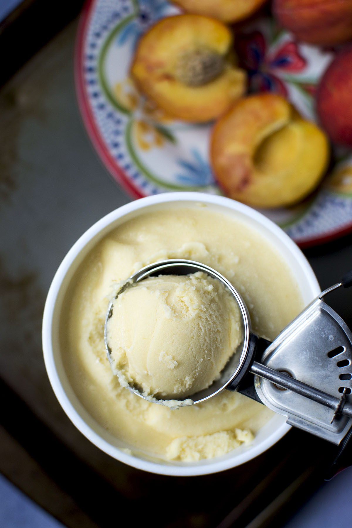 Ice cream in a scoop resting on a container with peaches in the background