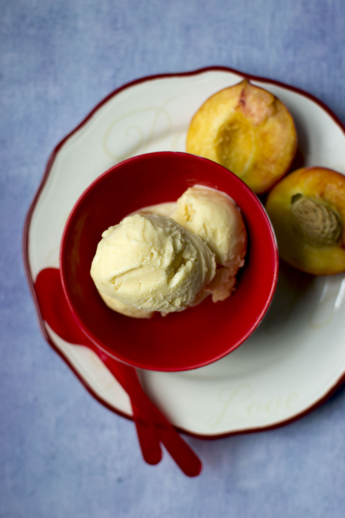 Red bowl with ice cream scoops and halved peaches on the side.