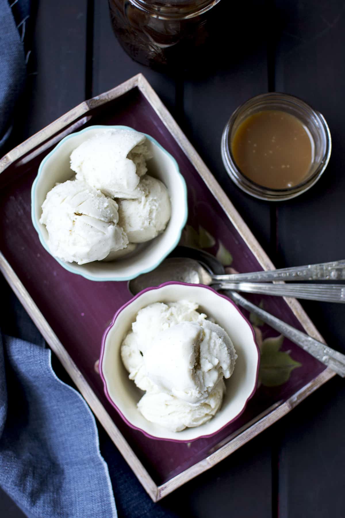 Painted bowls with scoops of sweet milk ice cream served on a tray with caramel sauce on the side