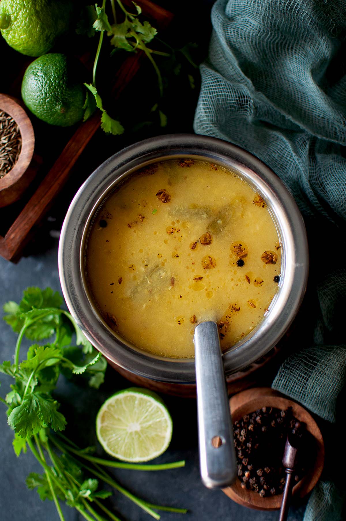 Steel bowl with lemon rasam with a steel spoon inside.