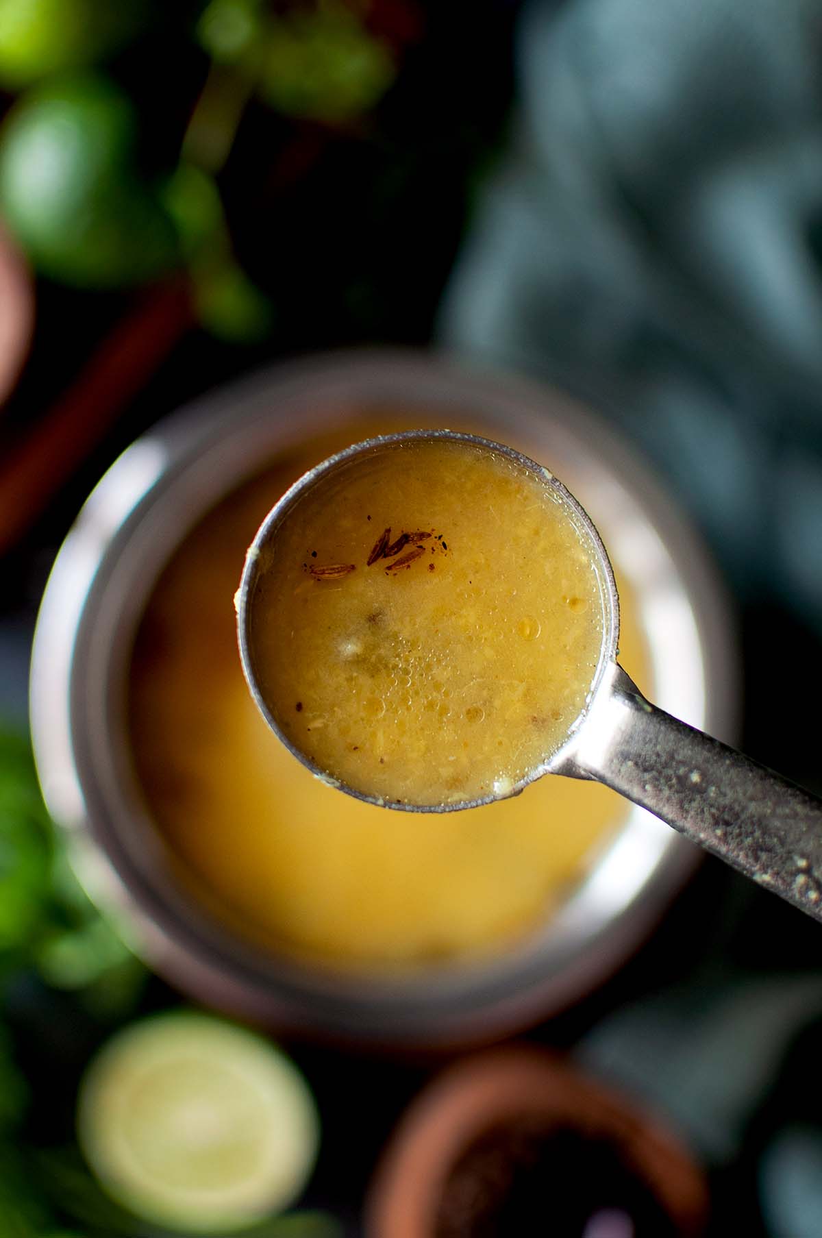 Steel spoon holding lemon rasam over a bowl.