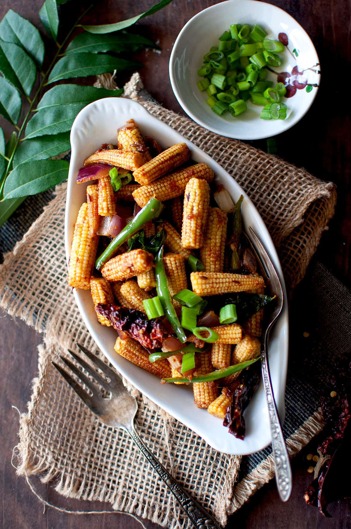 White bowl with roast baby corn topped with scallions.