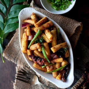 White bowl with roast baby corn topped with scallions.