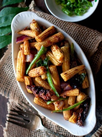 White bowl with roast baby corn topped with scallions.