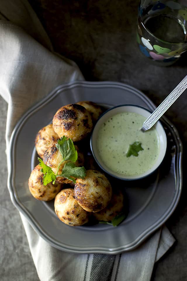 Grey plate with mixed vegetable paniyaram and a bowl of chutney