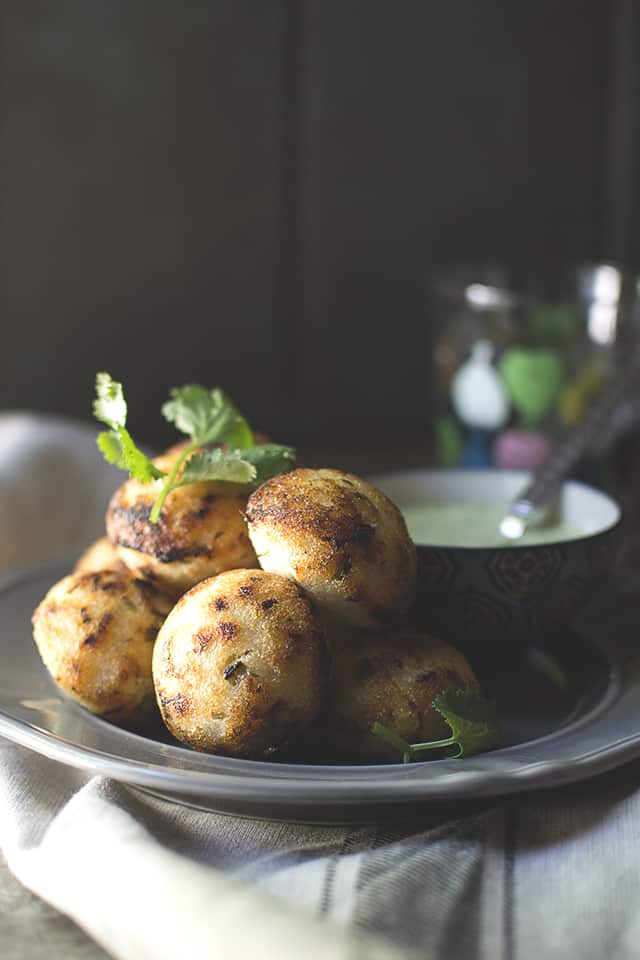 Grey plate with veggie ponganalu and a bowl of chutney in the background