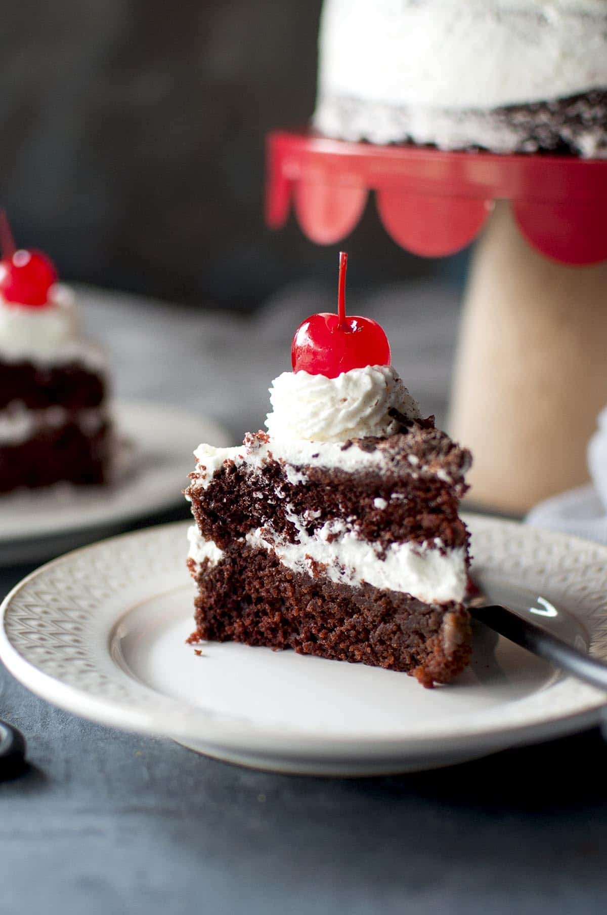 White plate with 2 layer frosted eggless Black Forest cake with a cherry on top