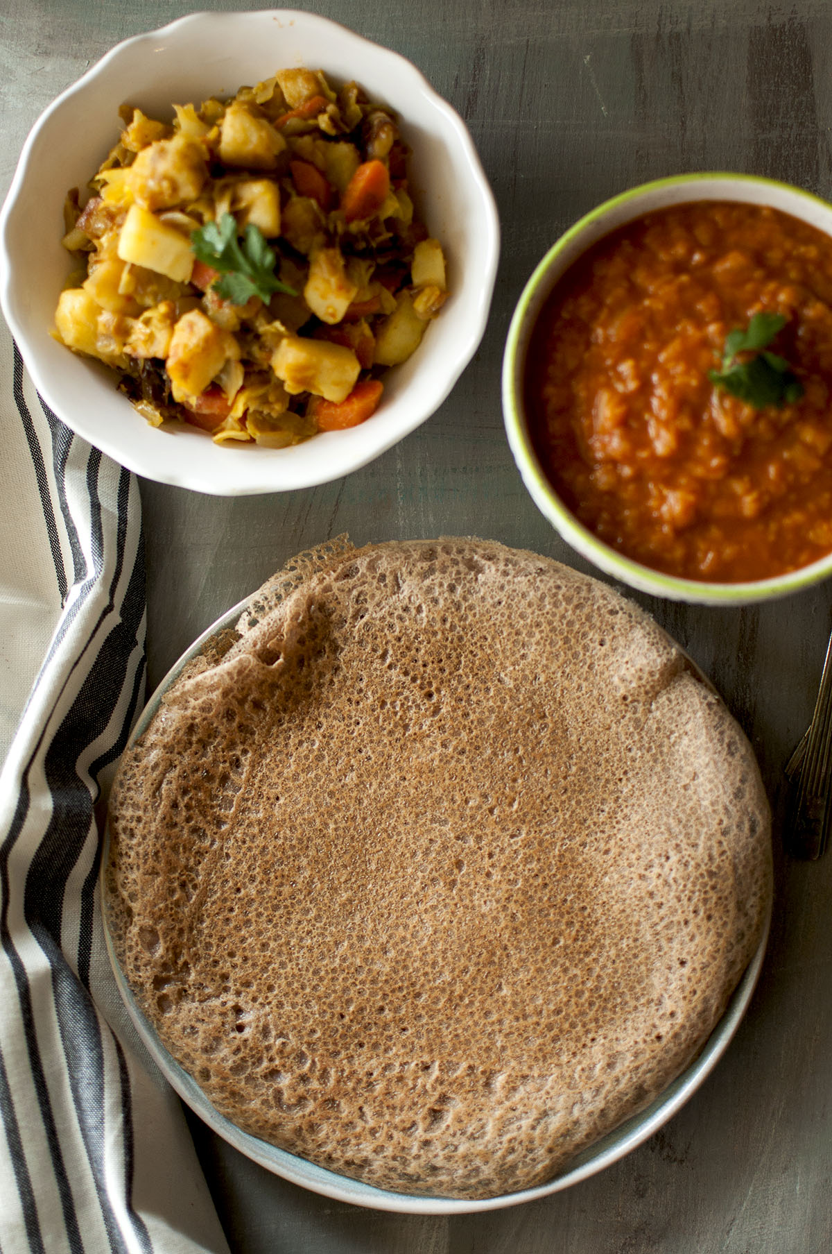 Plate with quick injera and bowls of curry and dal in the background.