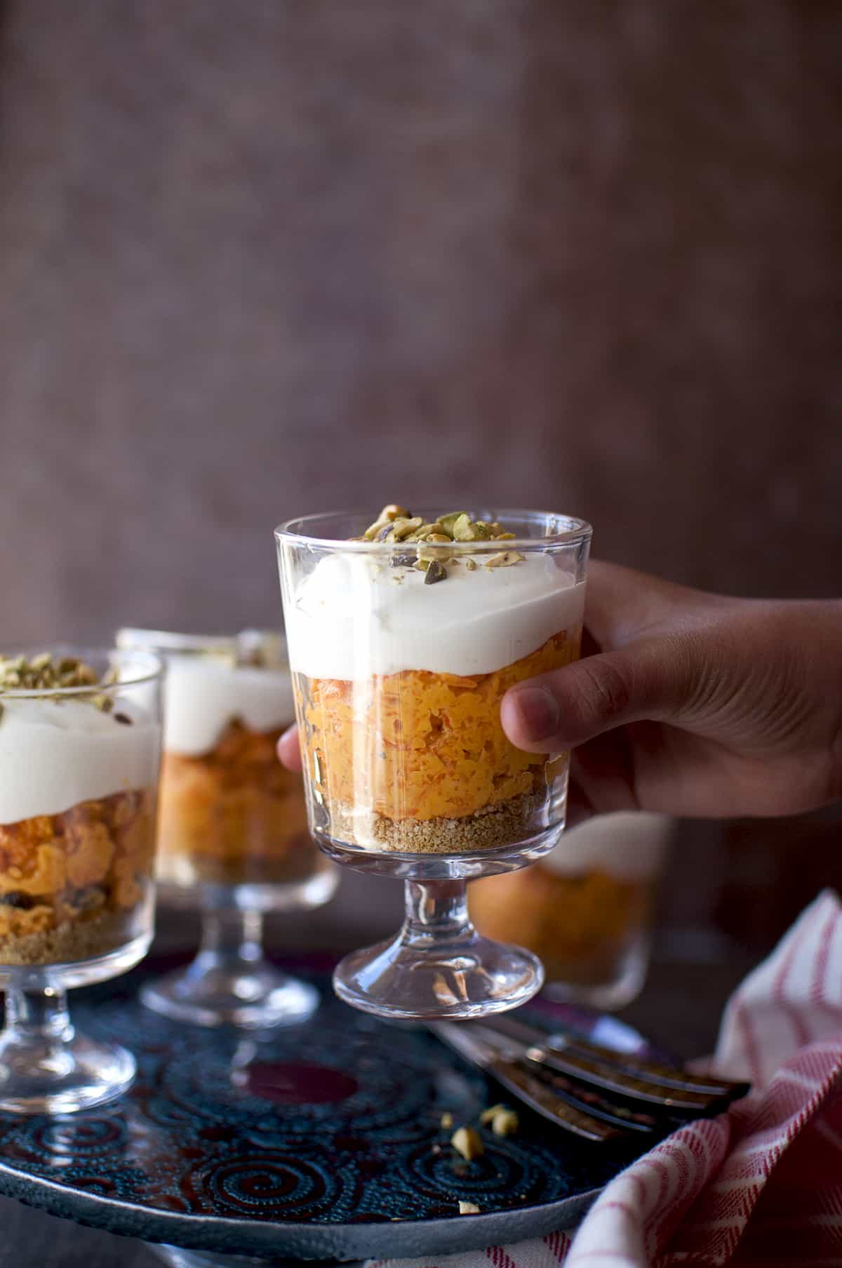 Hand holding a glass with carrot halwa cheesecake.