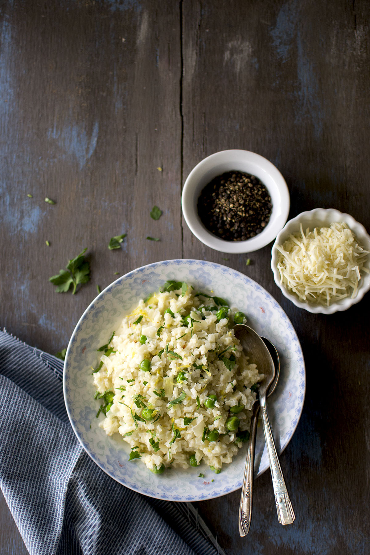 White bowl with Cauliflower risotto with small bowls with grated cheese and peppercorn