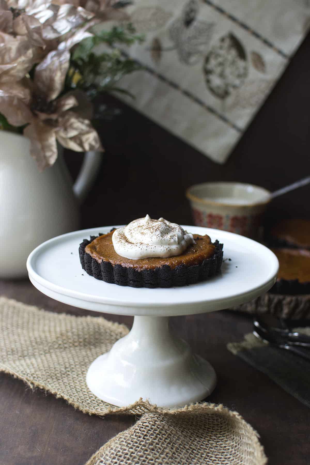 White cake stand with a whipped cream topped mini pumpkin pie