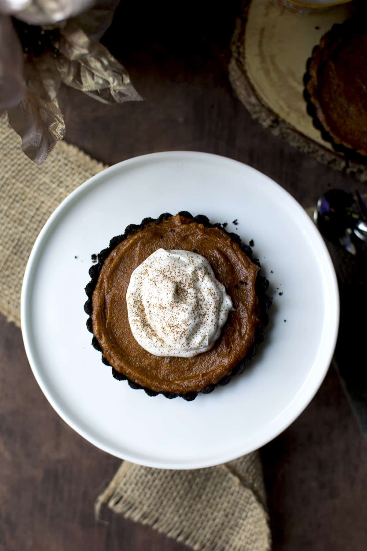 White cake plate with a mini pumpkin pie topped with whipped cream and ground cinnamon