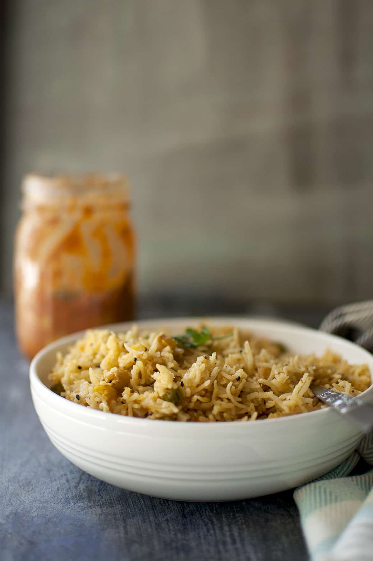 White bowl with achari vegetable pulao with a jar of pickle in the background