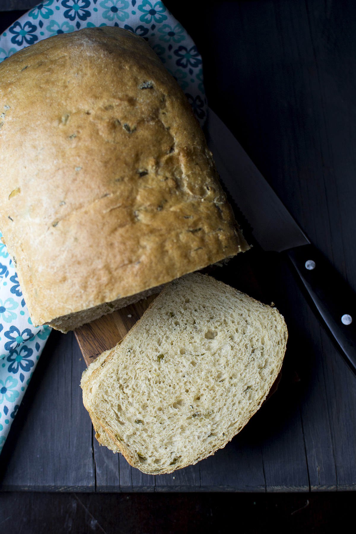 Chopping board with sliced chive bread along with a loaf