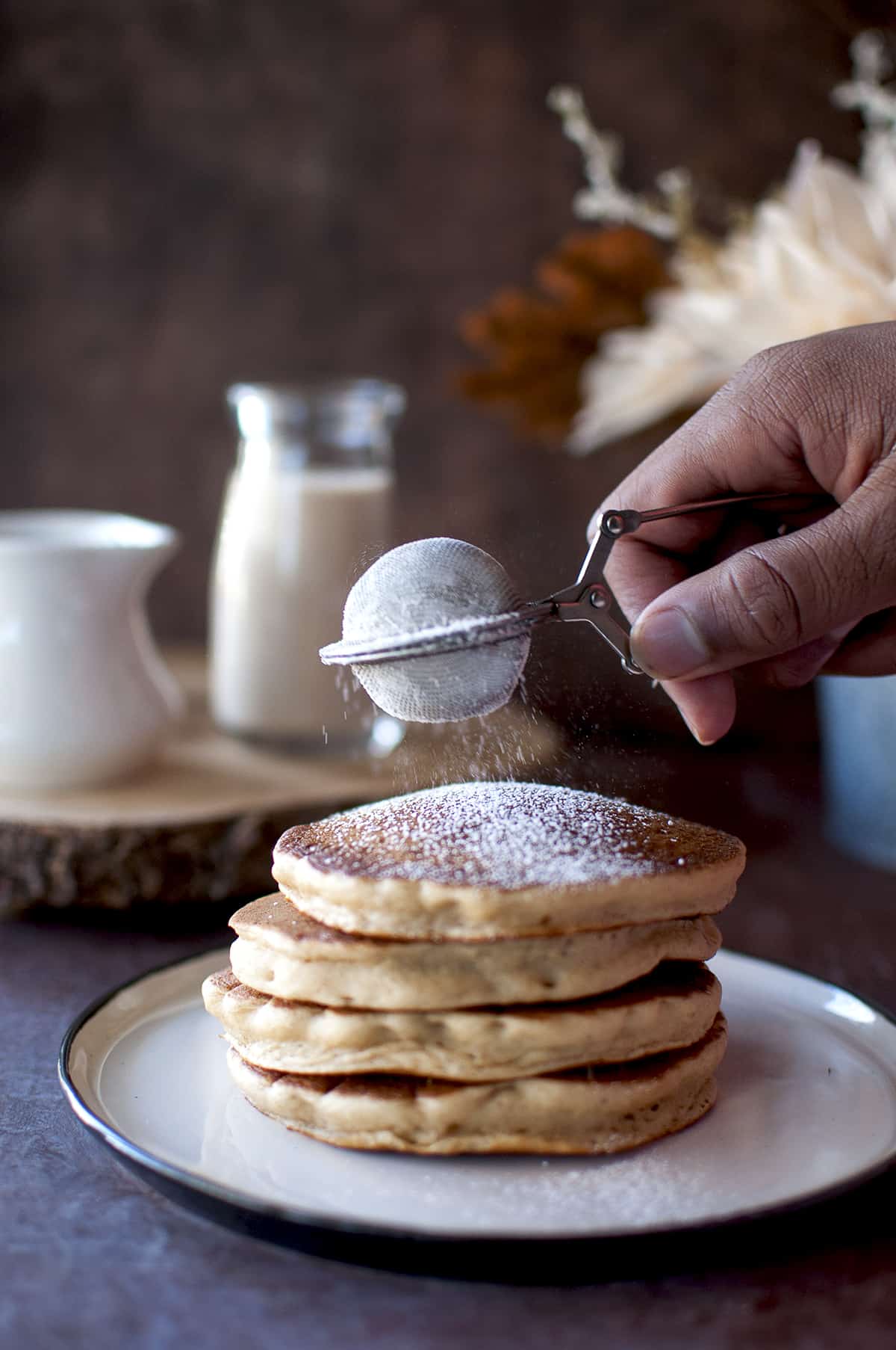 Hand sprinkling powdered sugar on a stack of pancakes