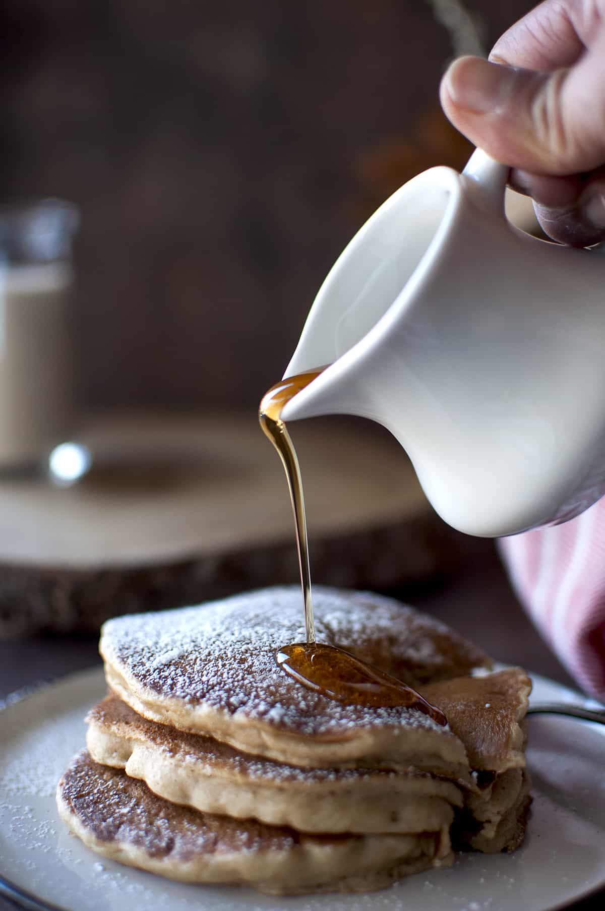 Hand pouring maple syrup on stack of vegan eggnog pancakes