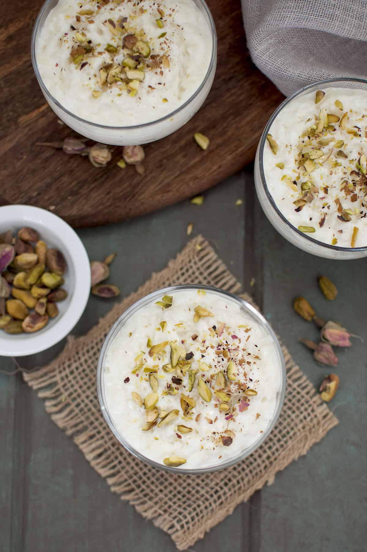 Top view of the dessert served in a glass serving bowl topped with chopped pistachio and dried rose buds