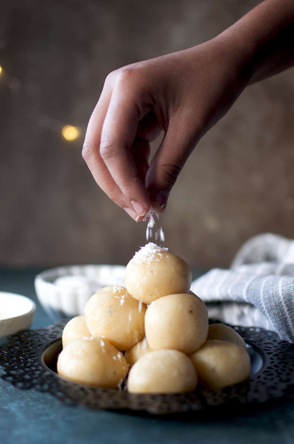 Hand sprinkling desiccated coconut on a stack of malai ladoo