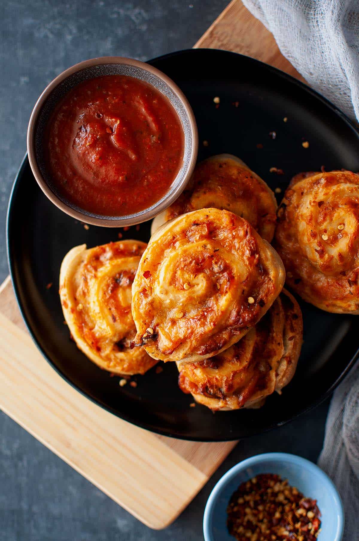 Black plate with a stack of pizza pinwheels and a bowl of marinara sauce.