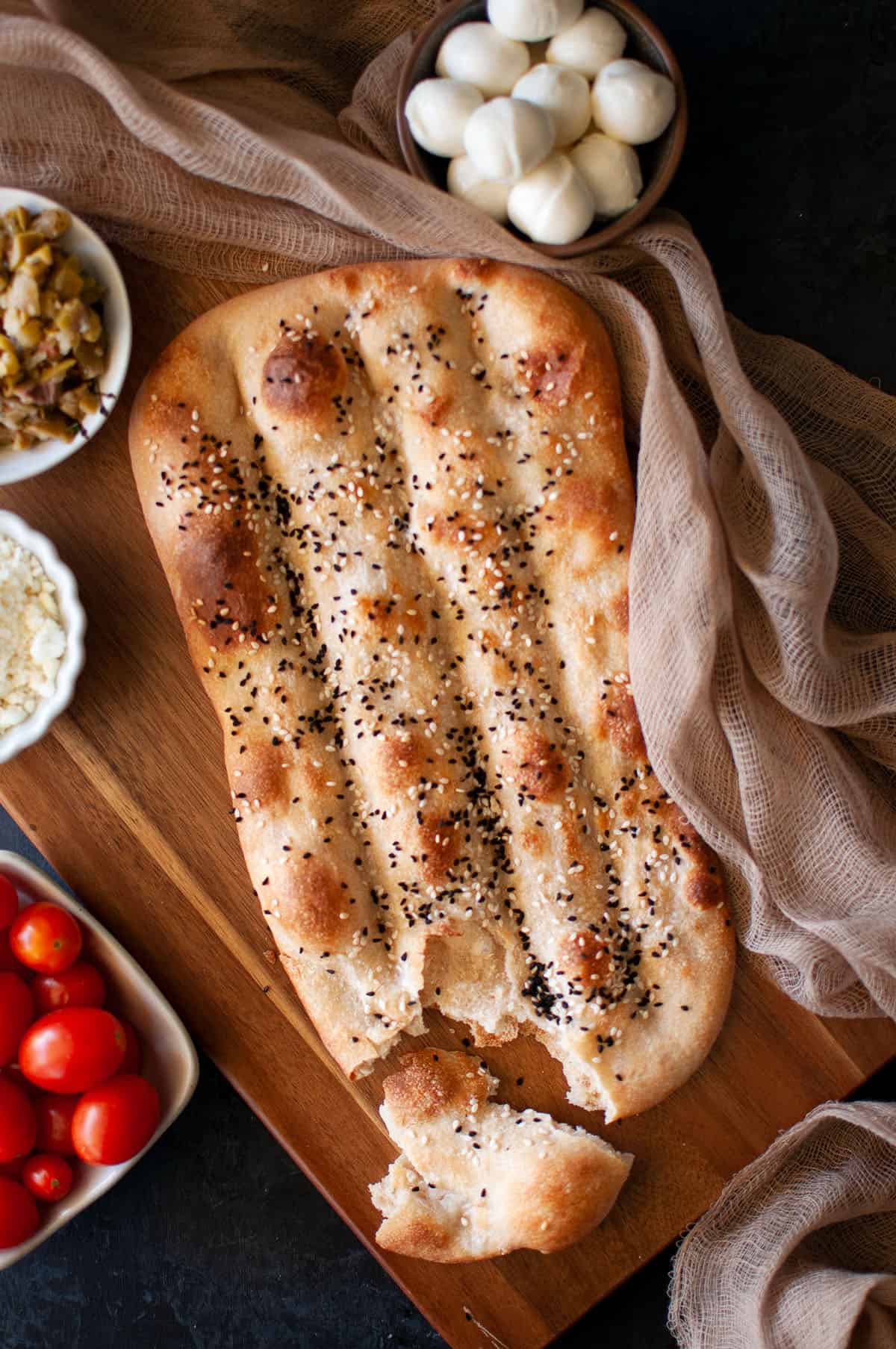 Wooden board with Naan e barbari bread with a corner broken.