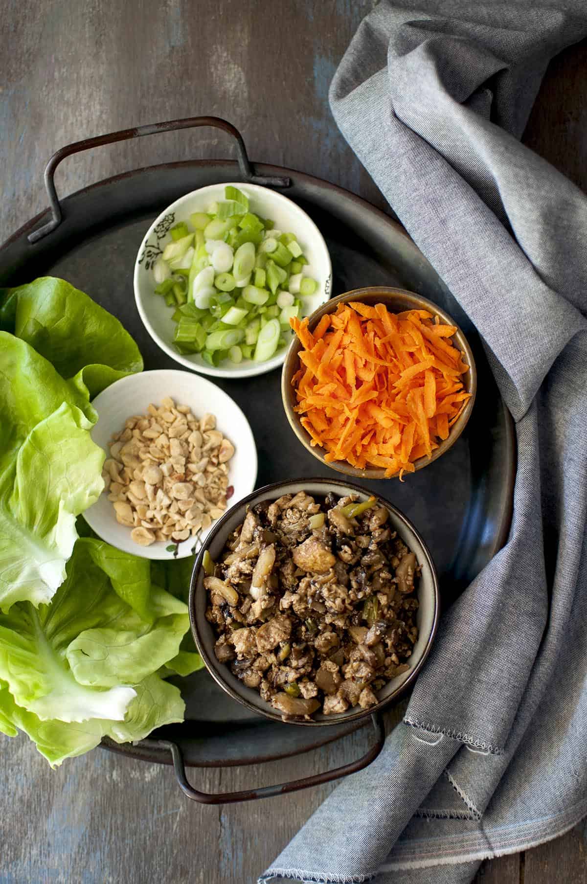 Tray with bowls of tofu mixture, grated carrot, peanuts and lettuce leaves