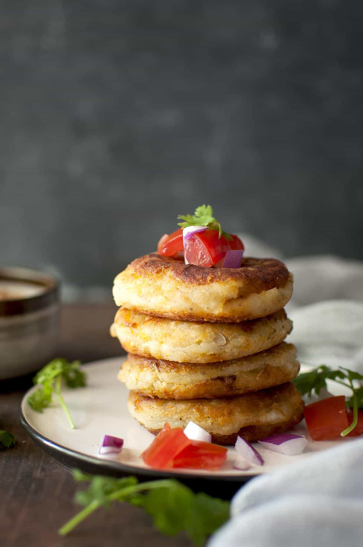 White plate with a stack of 4 Llapingachos topped with chopped tomatoes