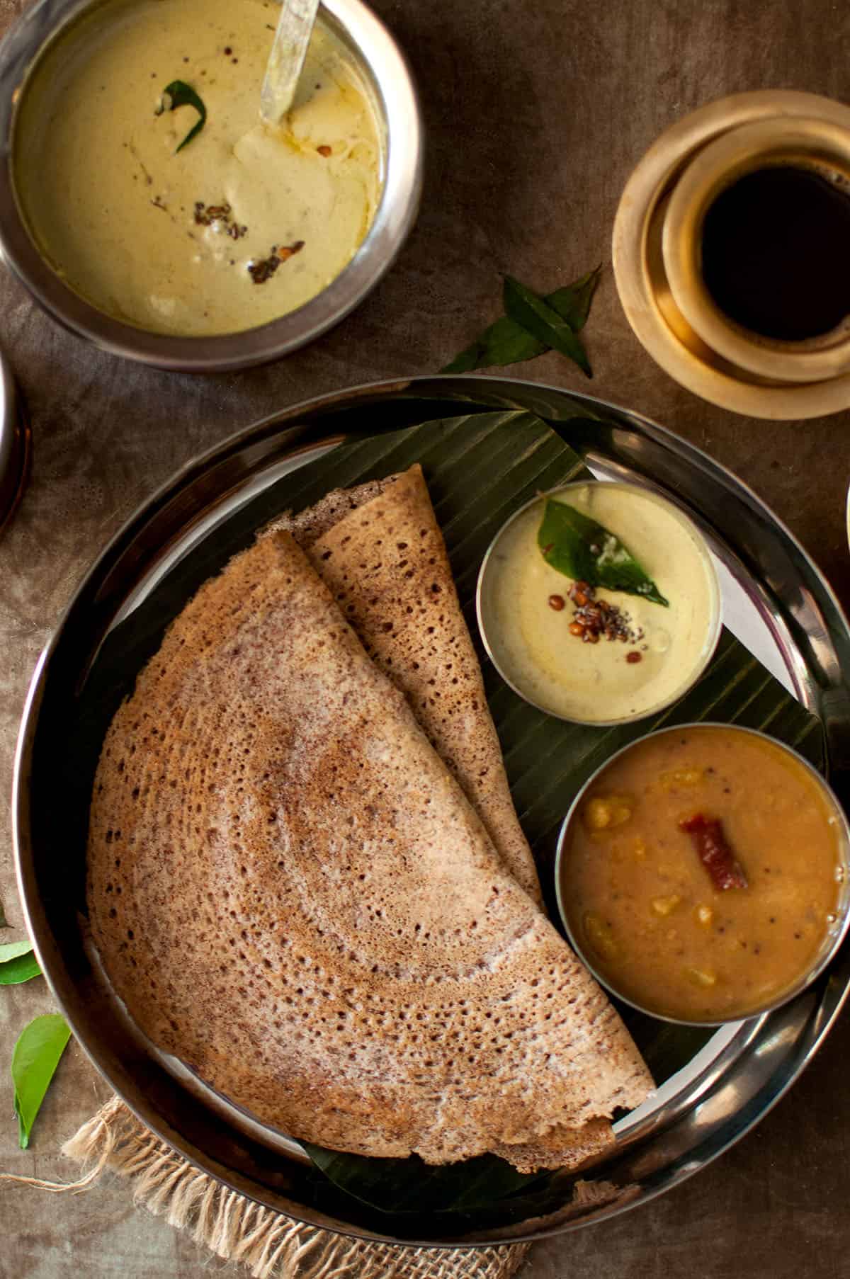 Steel plate with 2 sprouted ragi dosa and bowls of chutney and sambar.