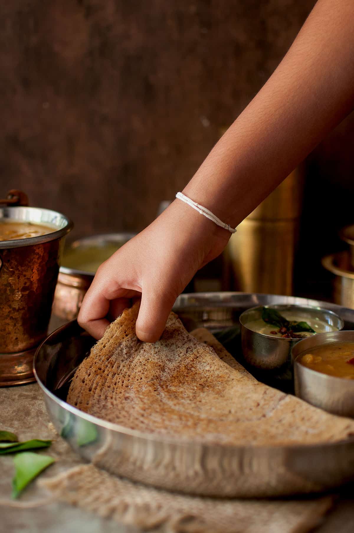 hand cutting a piece of dosa from a steel plate.