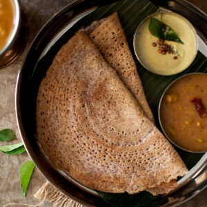 Steel plate with 2 sprouted ragi dosa and bowls of chutney and sambar.