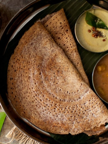 Steel plate with 2 sprouted ragi dosa and bowls of chutney and sambar.