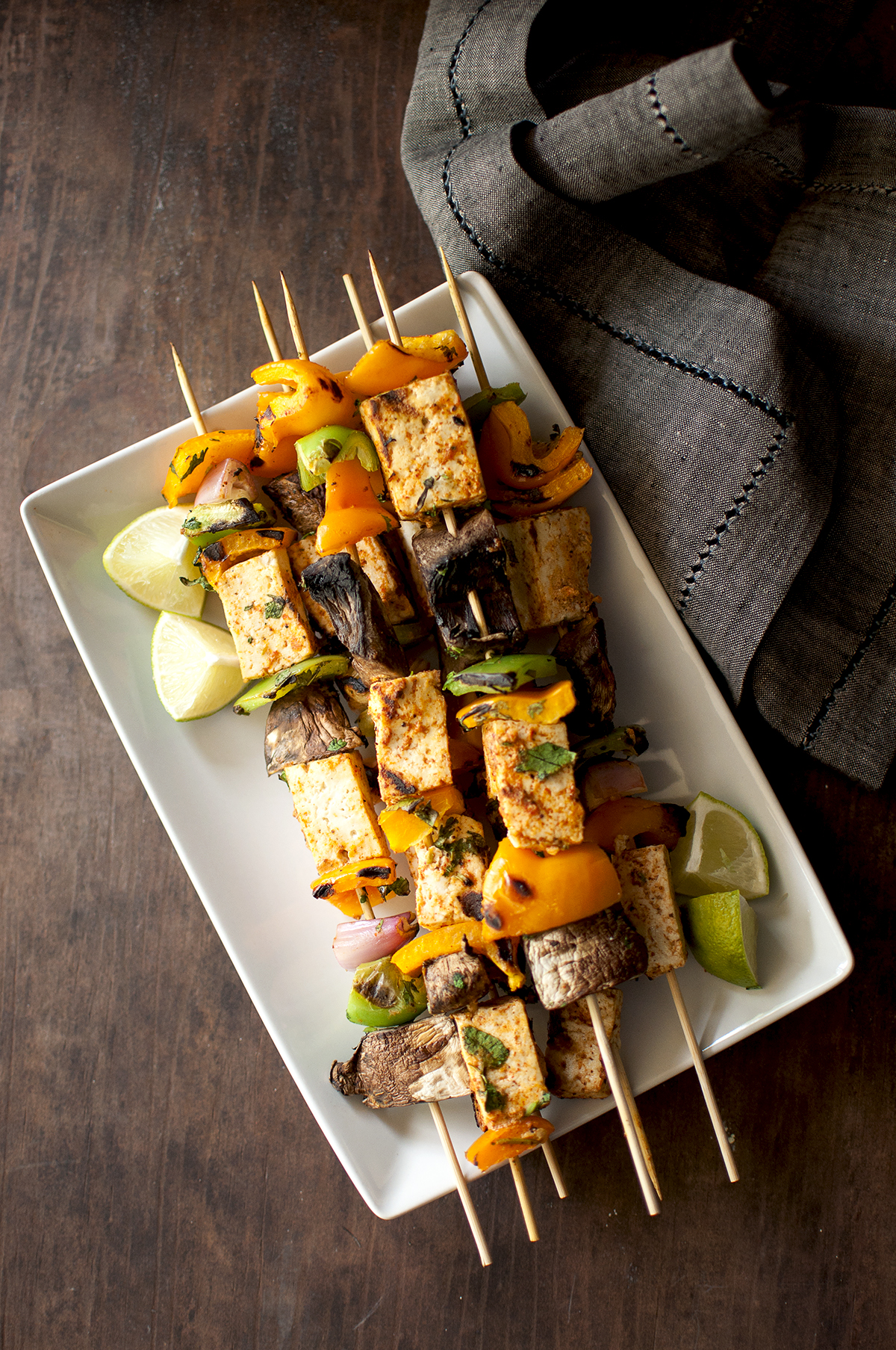 White platter with grilled tofu and vegetable skewers and lime wedges