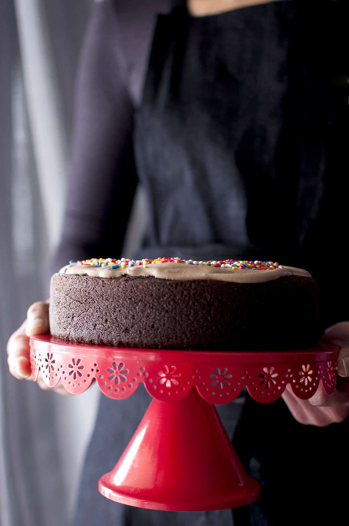 Baker holding a red cake stand with vegan chocolate beet cake