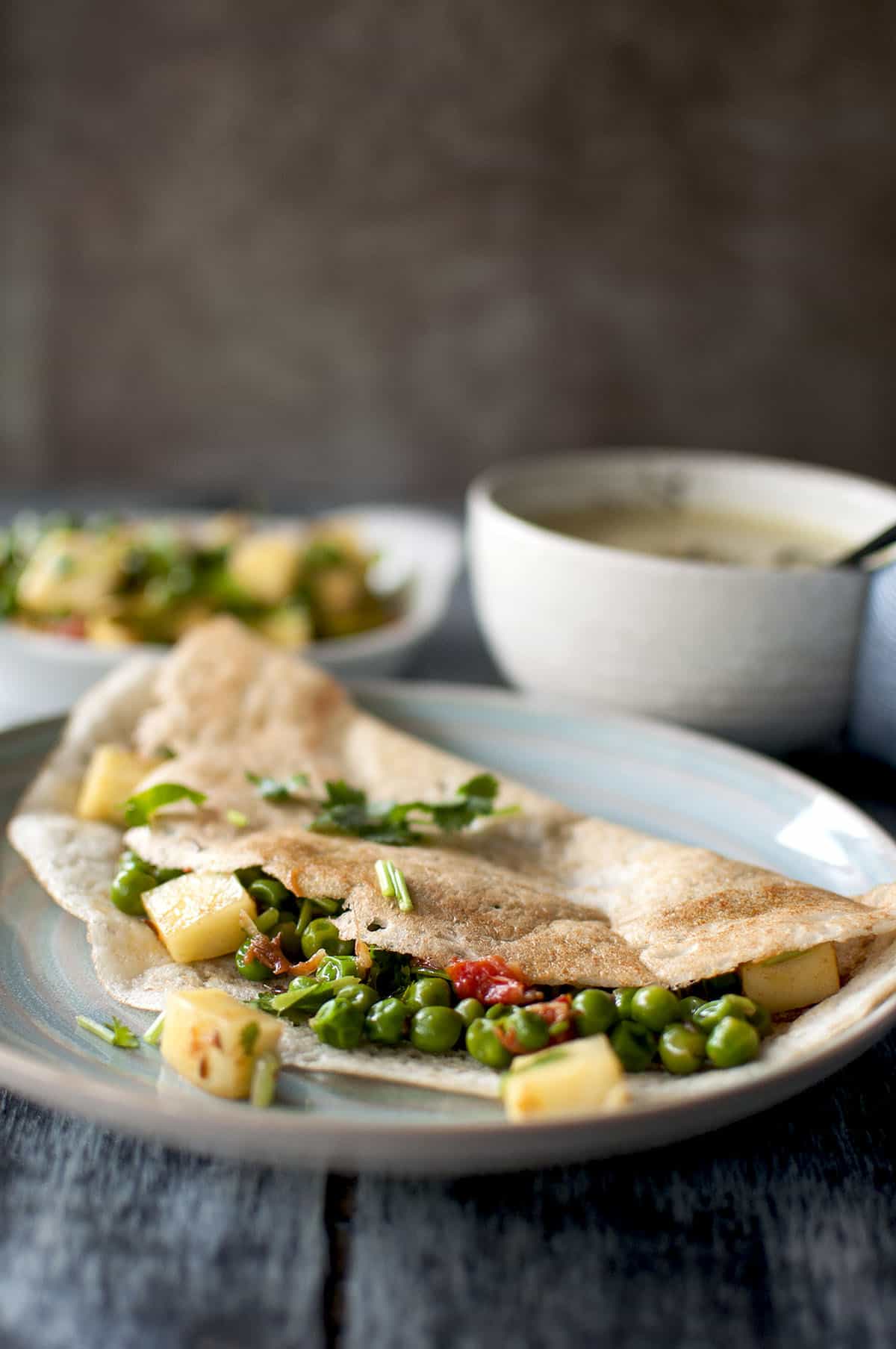 Blue plate with dosa filled with green peas and paneer cubes and topped with cilantro sprig