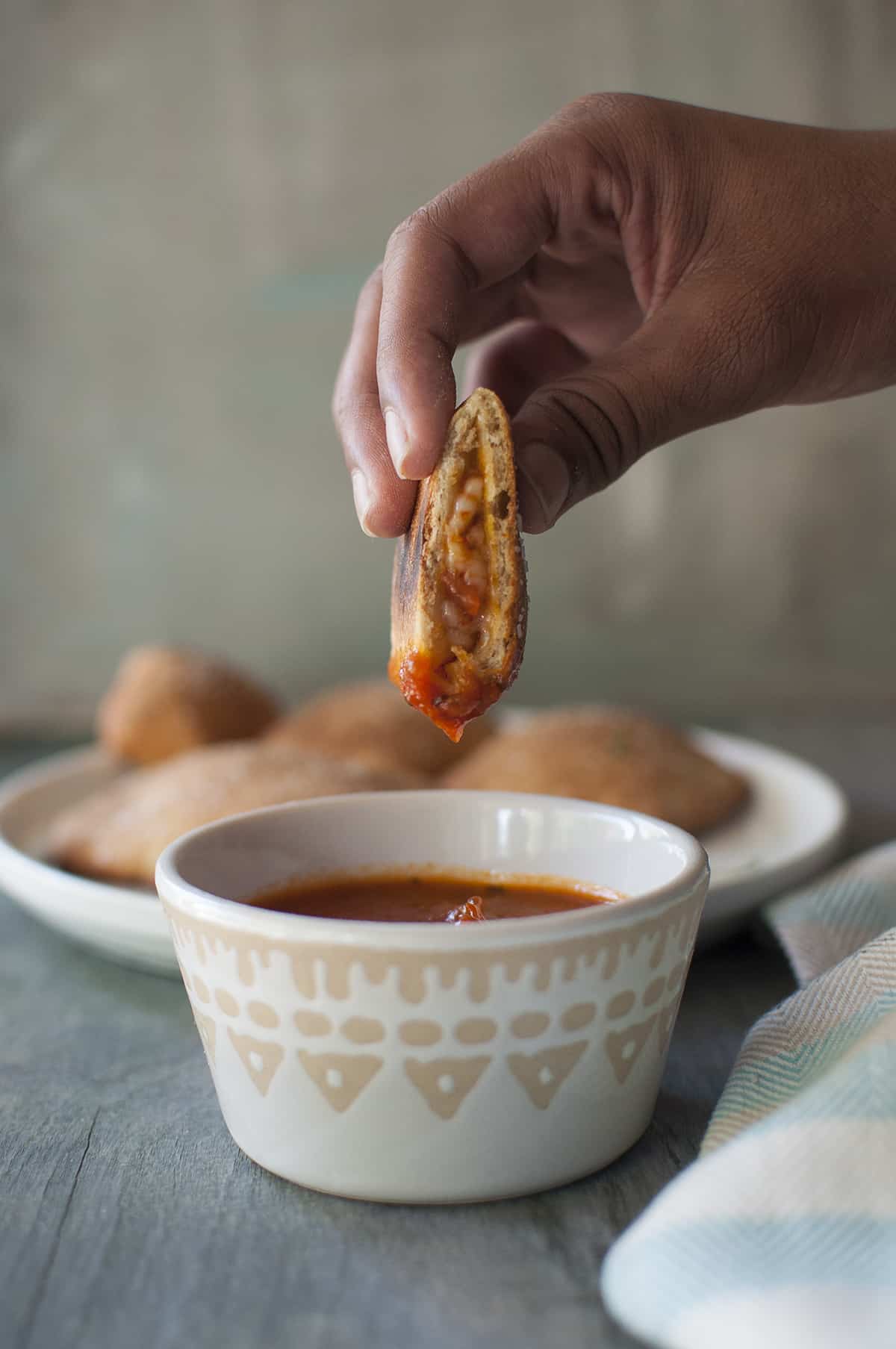 Hand holding popper being dipped in marinara sauce