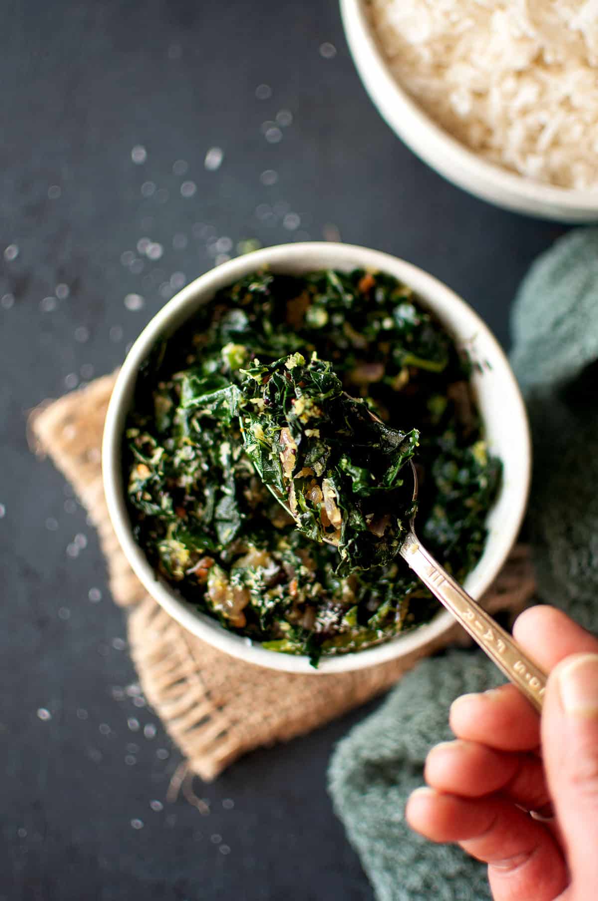 Hand holding kale dry curry over a bowl.