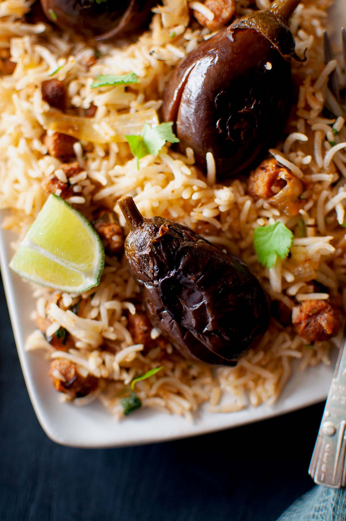 White plate with baby brinjal pulao and a lime wedge.