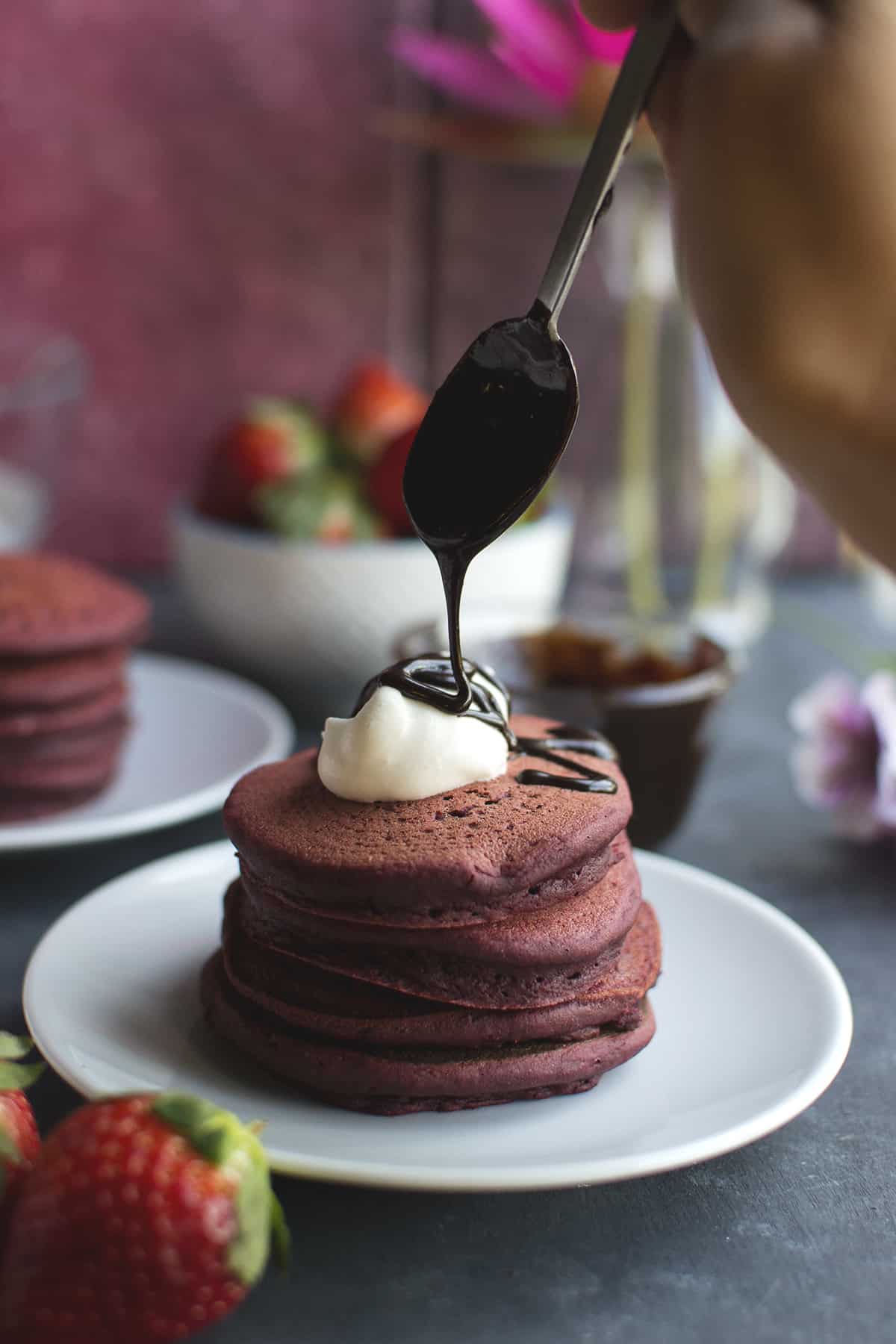 Pouring chocolate syrup on a stack of pancakes topped with whipped cream