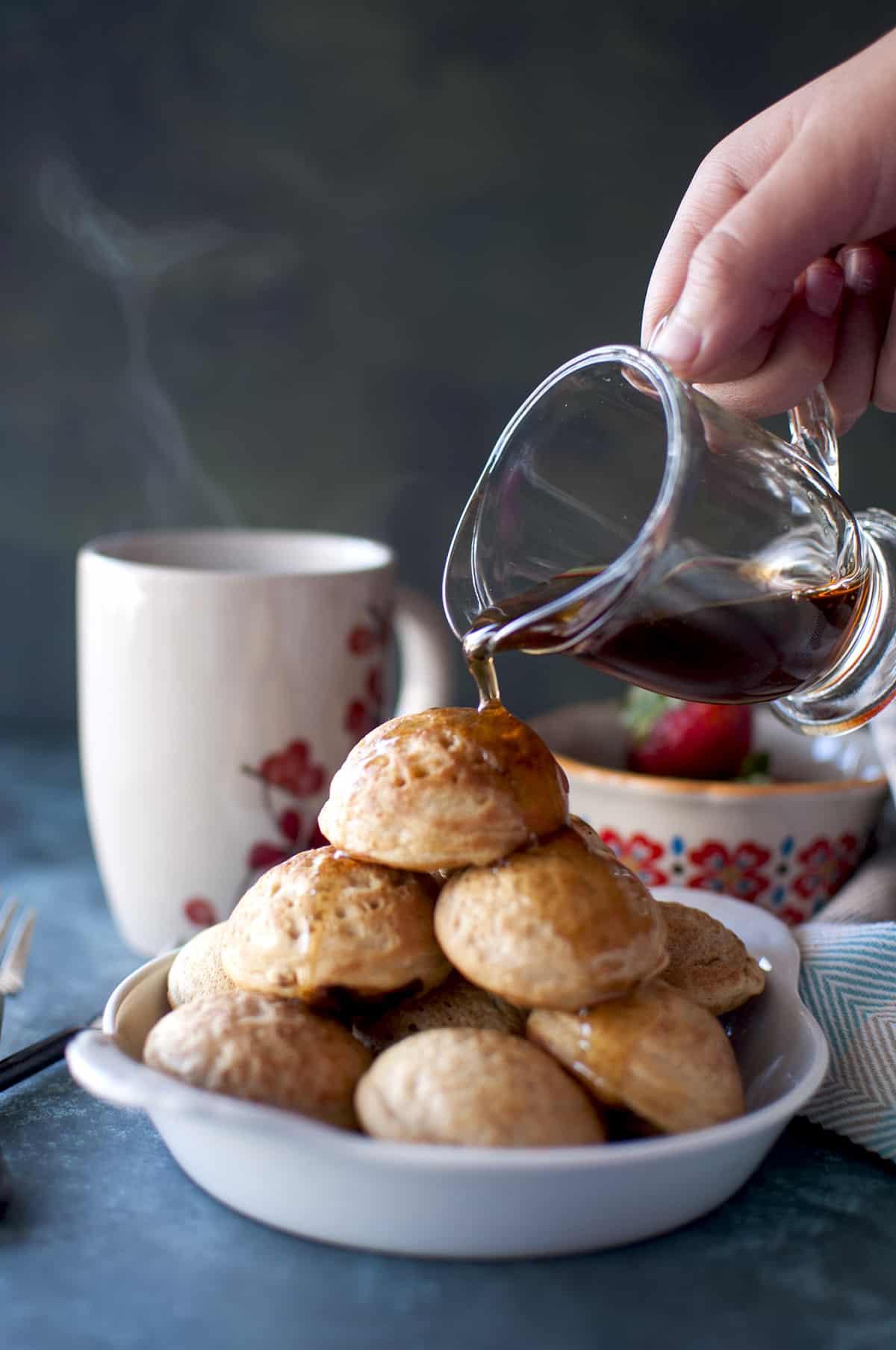 Hand pouring maple syrup onto a stack of vegan Danish aebliskivers