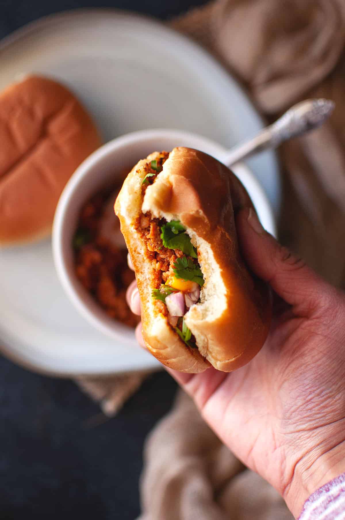 Hand holding a kheema pav sandwich.