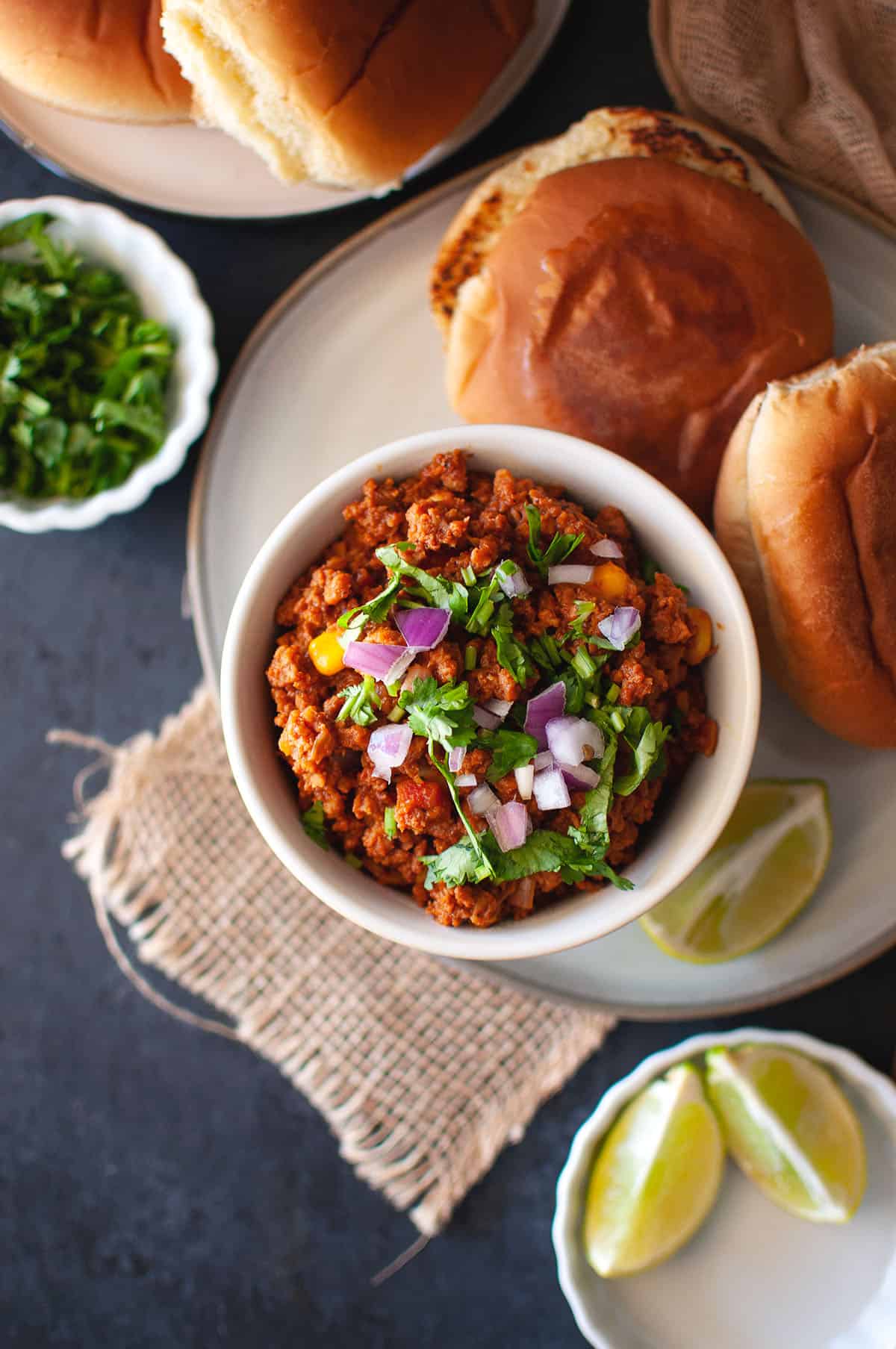 White bowl with vegan kheema topped with chopped onions and toasted pav on a plate.