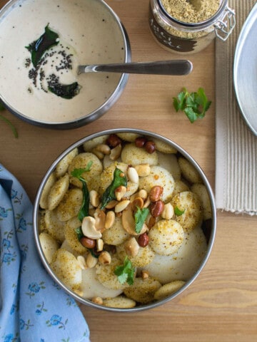 Top view of steel bowl with mini idly topped with peanuts and cashews.