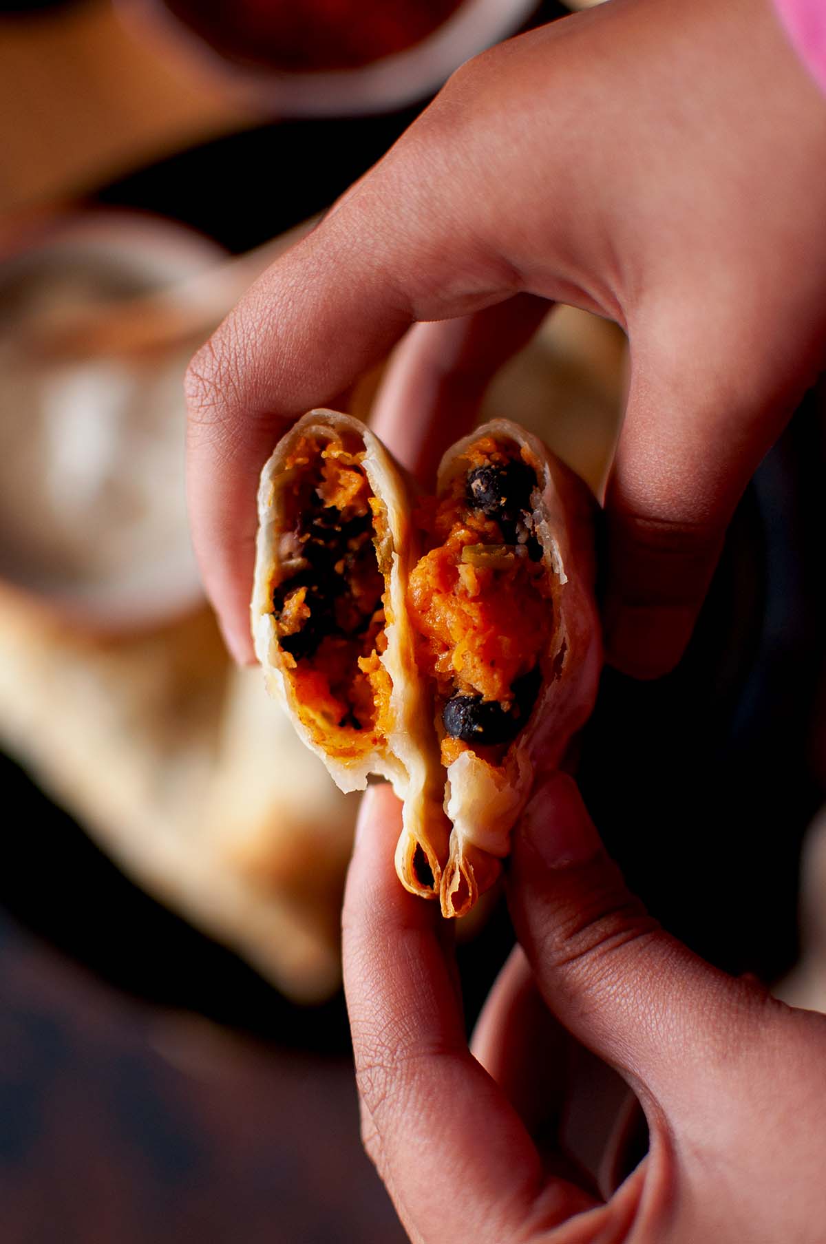 Hand holding a halved empanada showing sweet potato filling