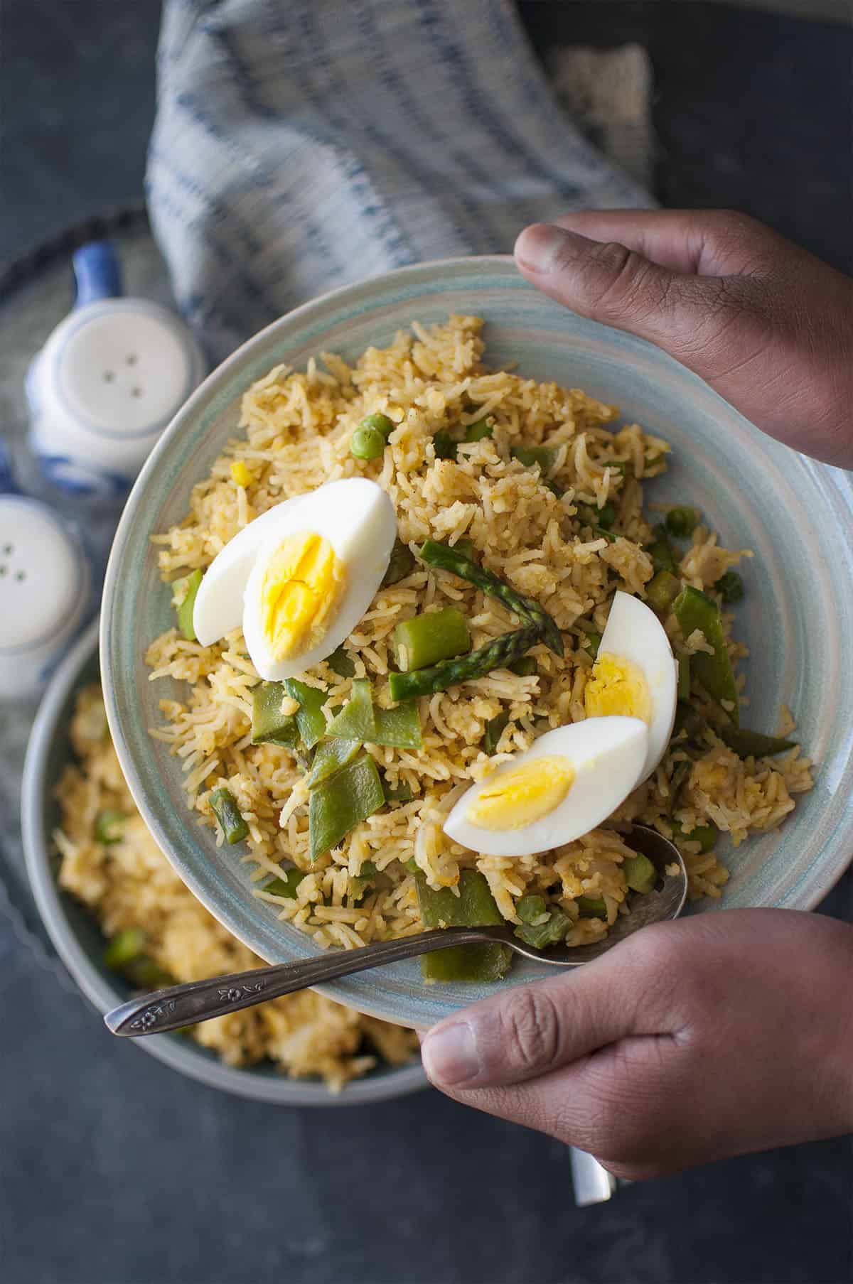 Hand holding blue plate with kedgeree topped with boiled eggs